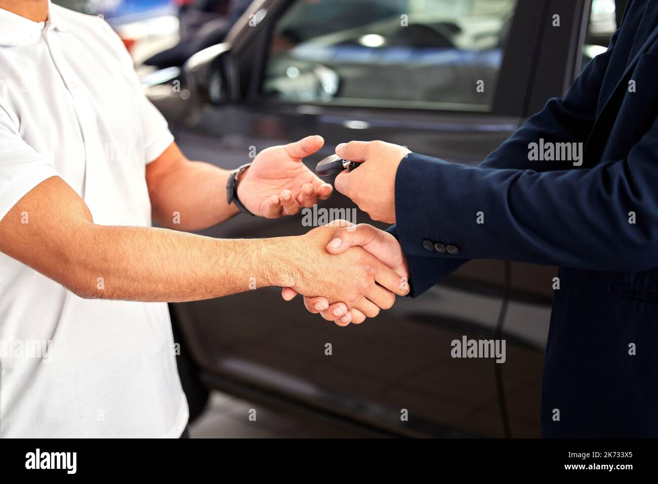 Congratulations on your new ride. a car salesman handing over keys and shaking his customers hand. Stock Photo