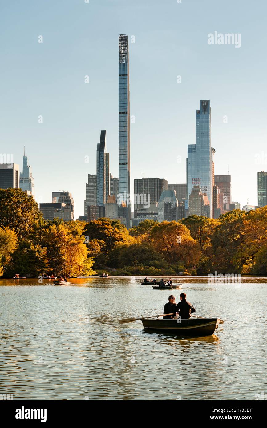 New York Central Park Lake in autumn with people rowing boats and view of Billionaires Row skyscrapers (Steinway Tower and One57). Midtown Manhattan Stock Photo