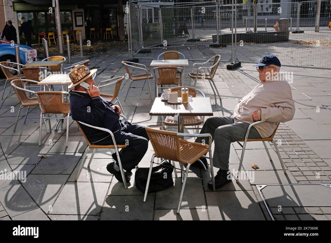 Two old aged male pensioners drinking at a cafe in Weston Super Mare, UK. One is talking on his phone. Stock Photo