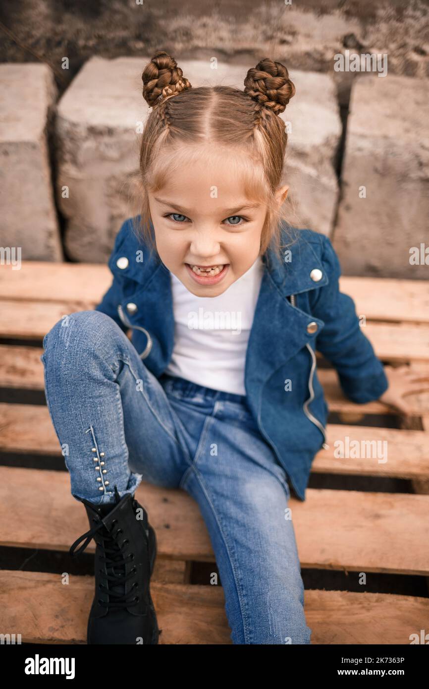 A beautiful little girl is sitting in stylish clothes on wooden pallets