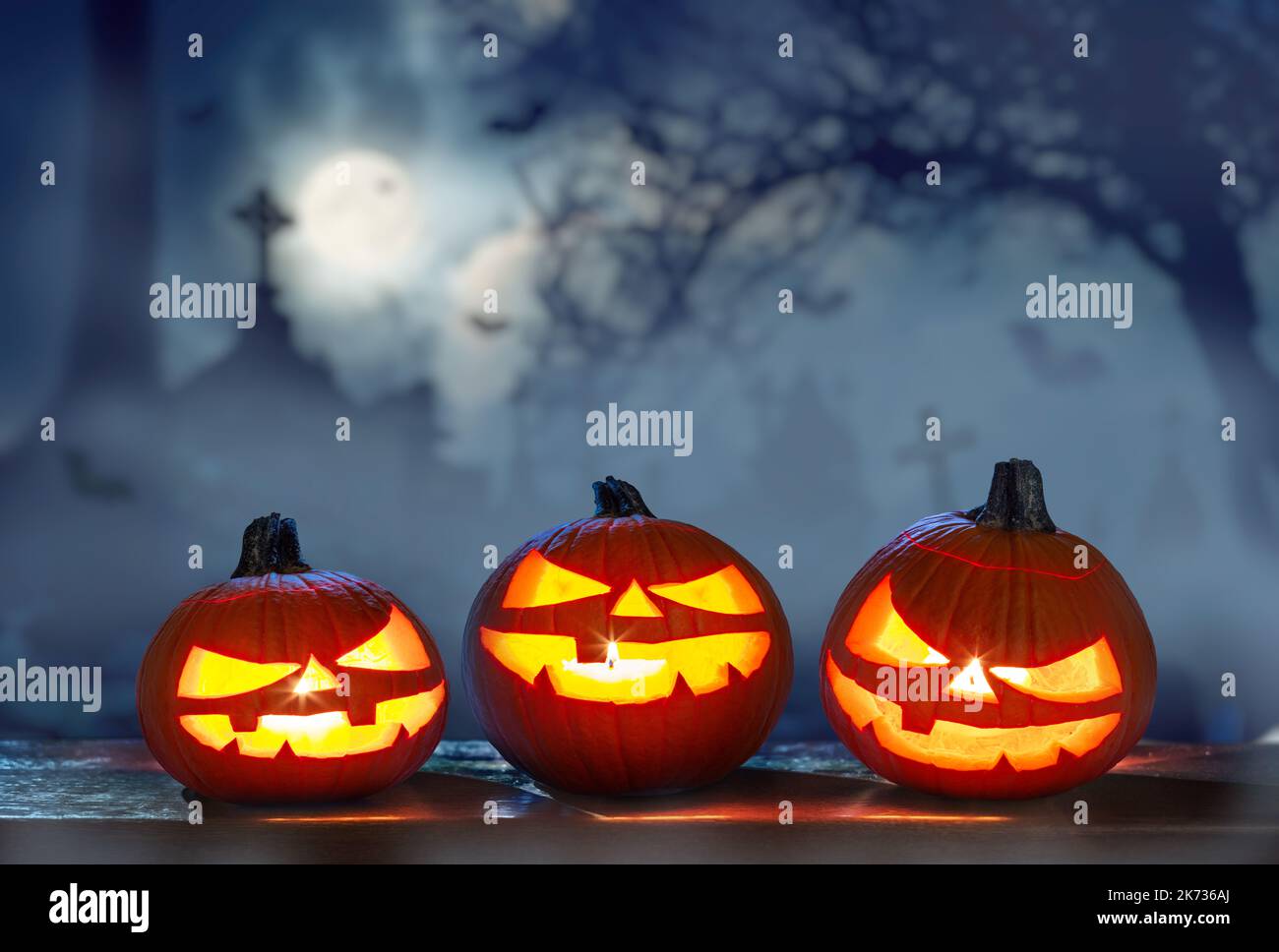 Carved lightening pumpkins for Halloween jack-o'-lanterns with scary smiles to ward of evil spirits on mystery night cemetery background. Halloween ba Stock Photo