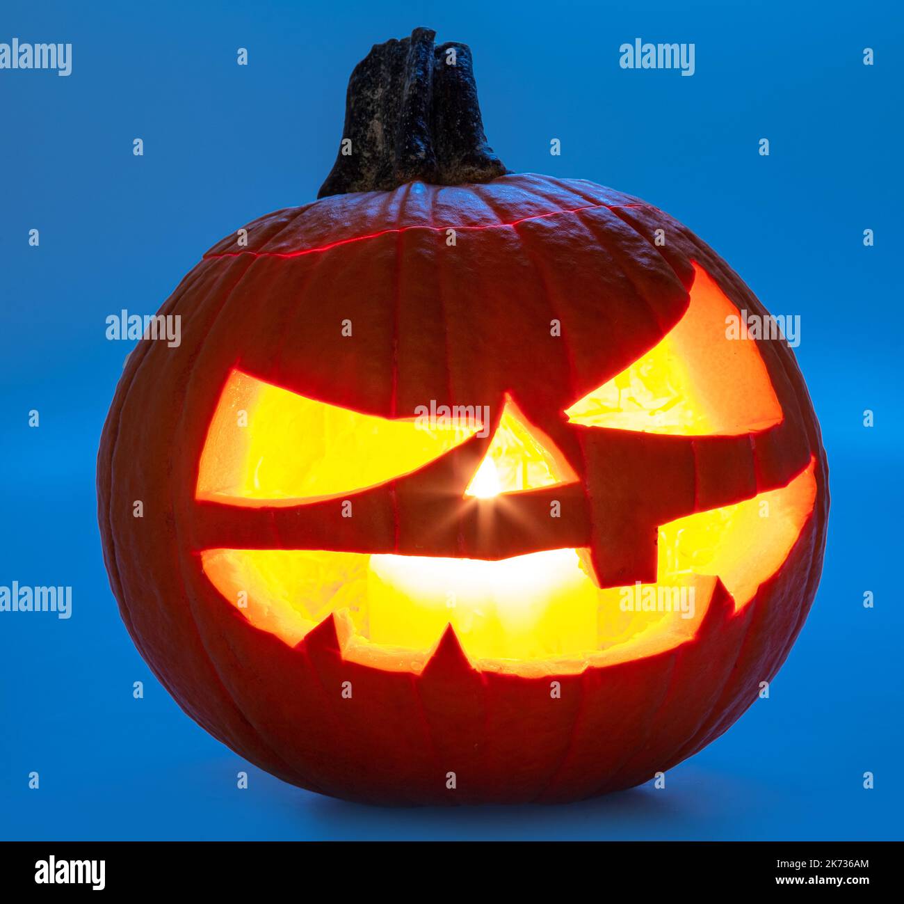 Carved pumpkin for Halloween jack-o'-lanterns with scary smiles and burning candle inside isolated on blue background. Stock Photo