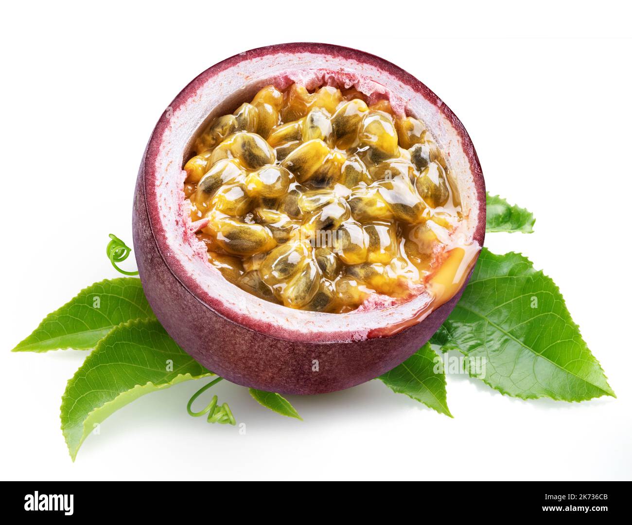 Dark purple passion fruit half with seedy interior laying on green passiflora leaves on white background. Stock Photo