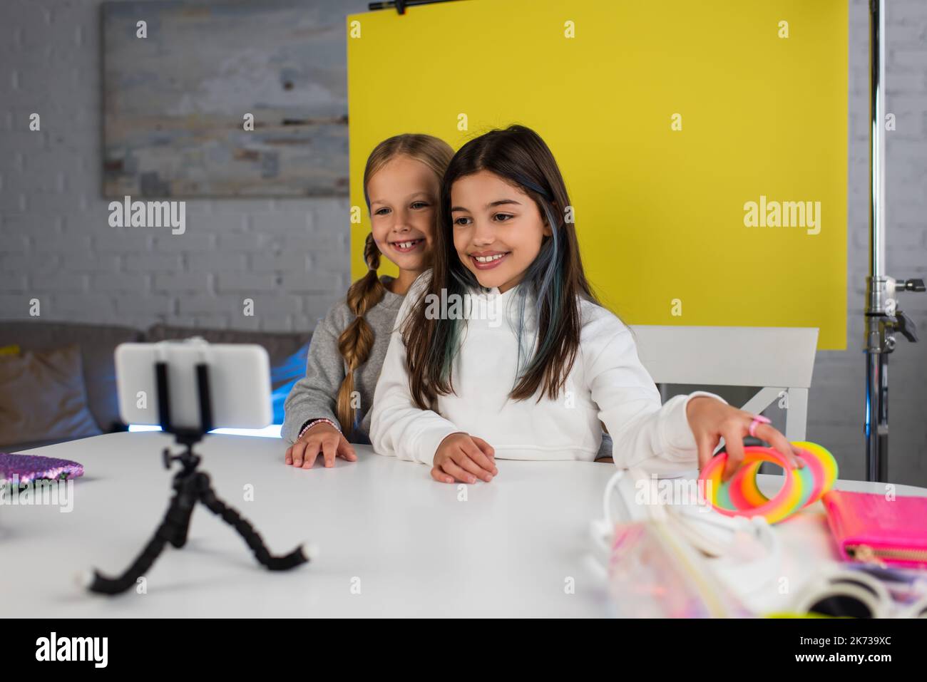 happy-preteen-bloggers-looking-at-blurred-smartphone-on-holder-while