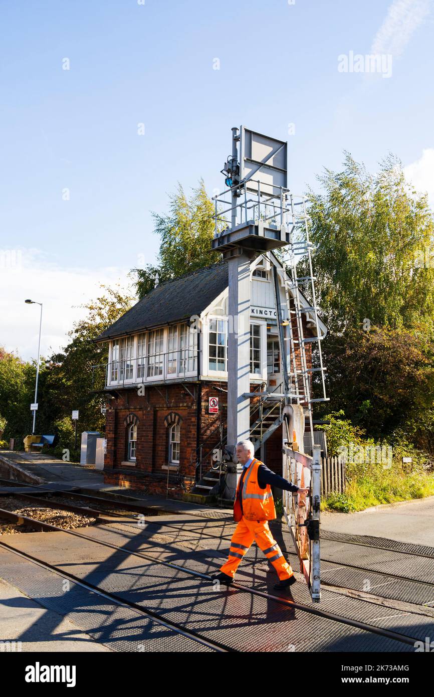 Railway worker closing the old manual level crossing gates, Station, signal box and manual level crossing. Heckington village, Lincolnshire, England. Stock Photo