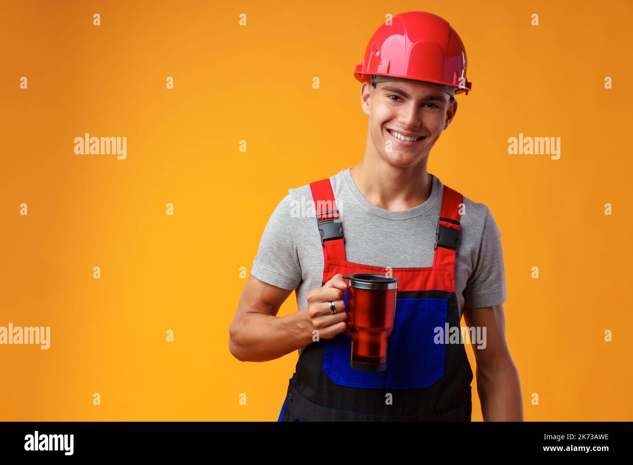 Young builder in uniform holding coffee cup on yellow background Stock Photo
