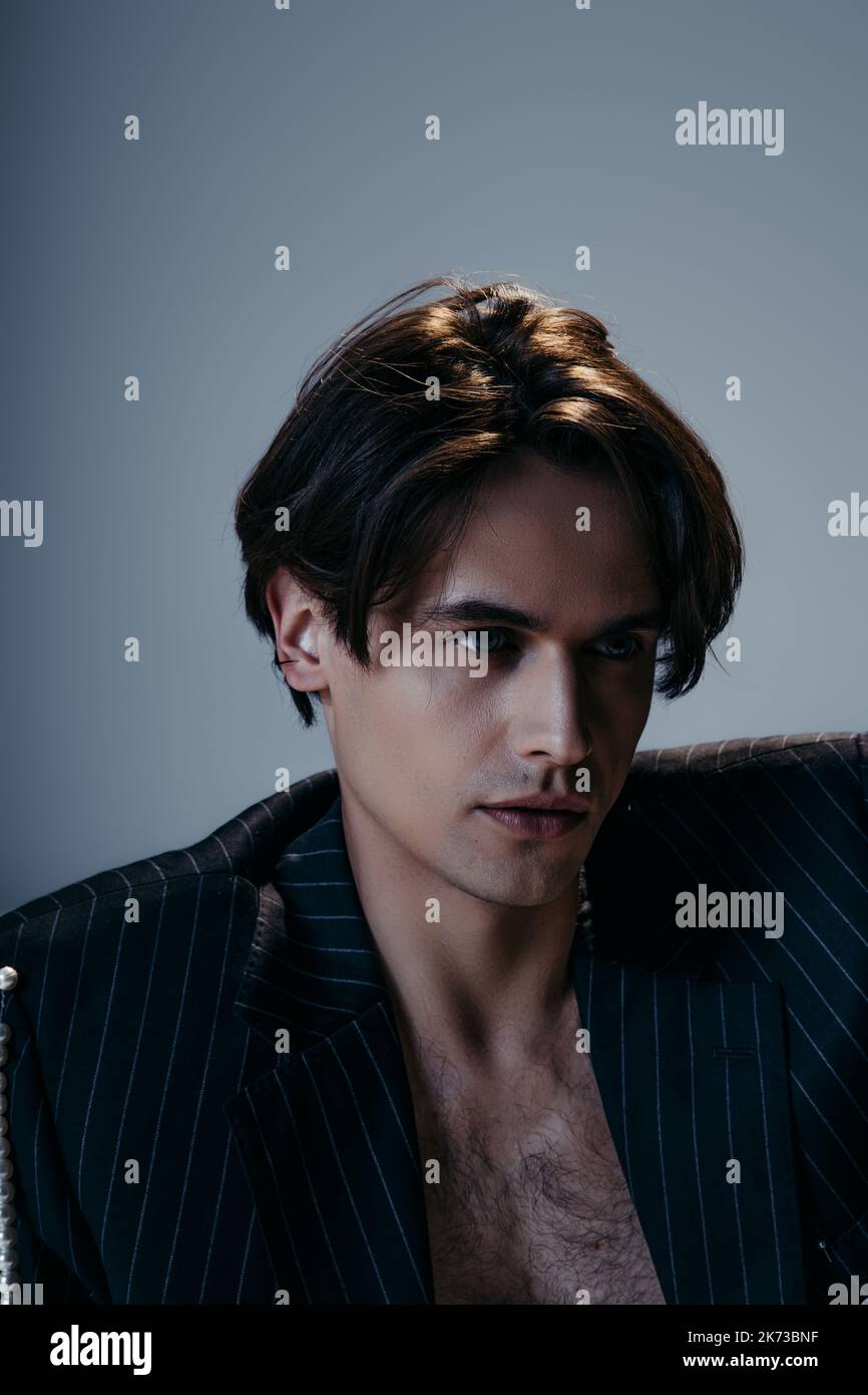 stylish man in striped jacket and hairy chest looking away on dark grey