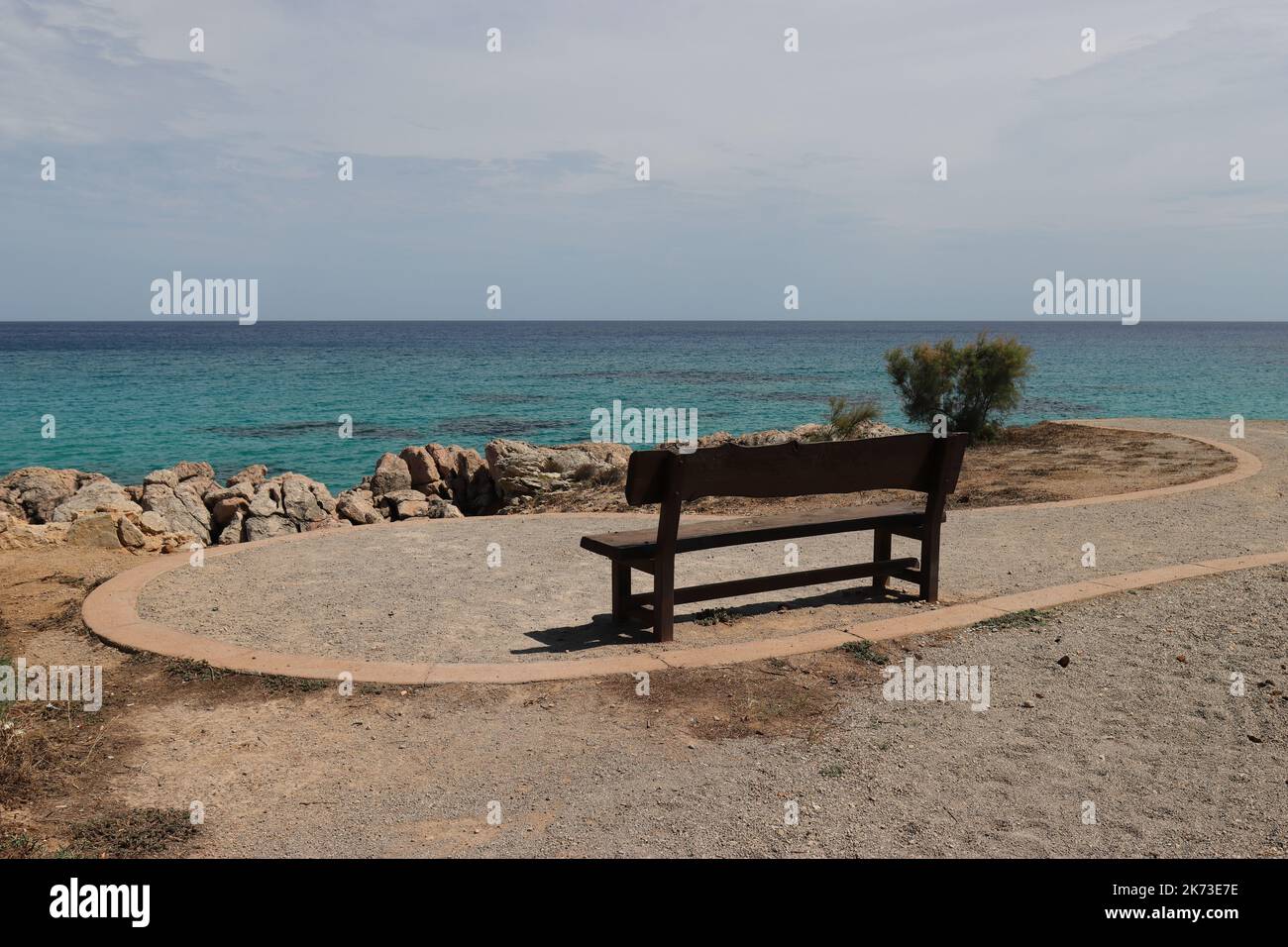 with a direct view of the sea, a small wooden bench stands on a beach promenade and is waiting for walkers, copy space Stock Photo
