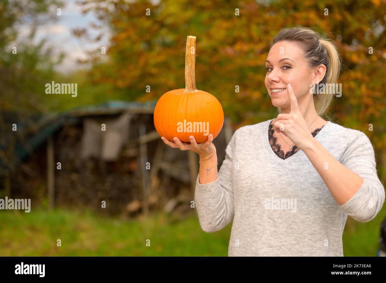 Pretty middle aged woman holding a small pumpkin in her hand and pointing her finger in the air like a teacher everyone pays attention against an autu Stock Photo