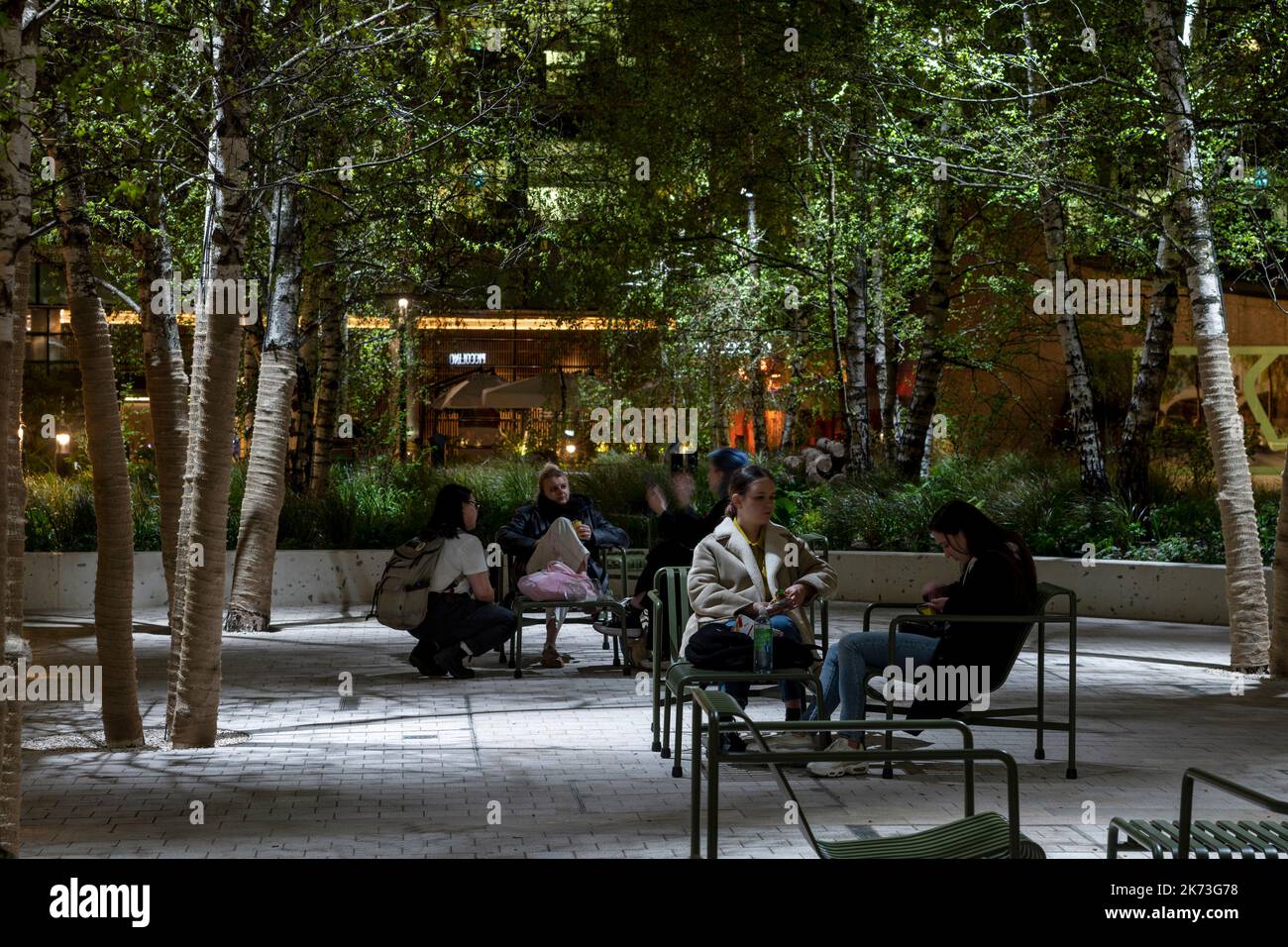 Seating area below trees with dappled lighting. Exchange Square, London, United Kingdom. Architect: DSDHA, 2022. Stock Photo
