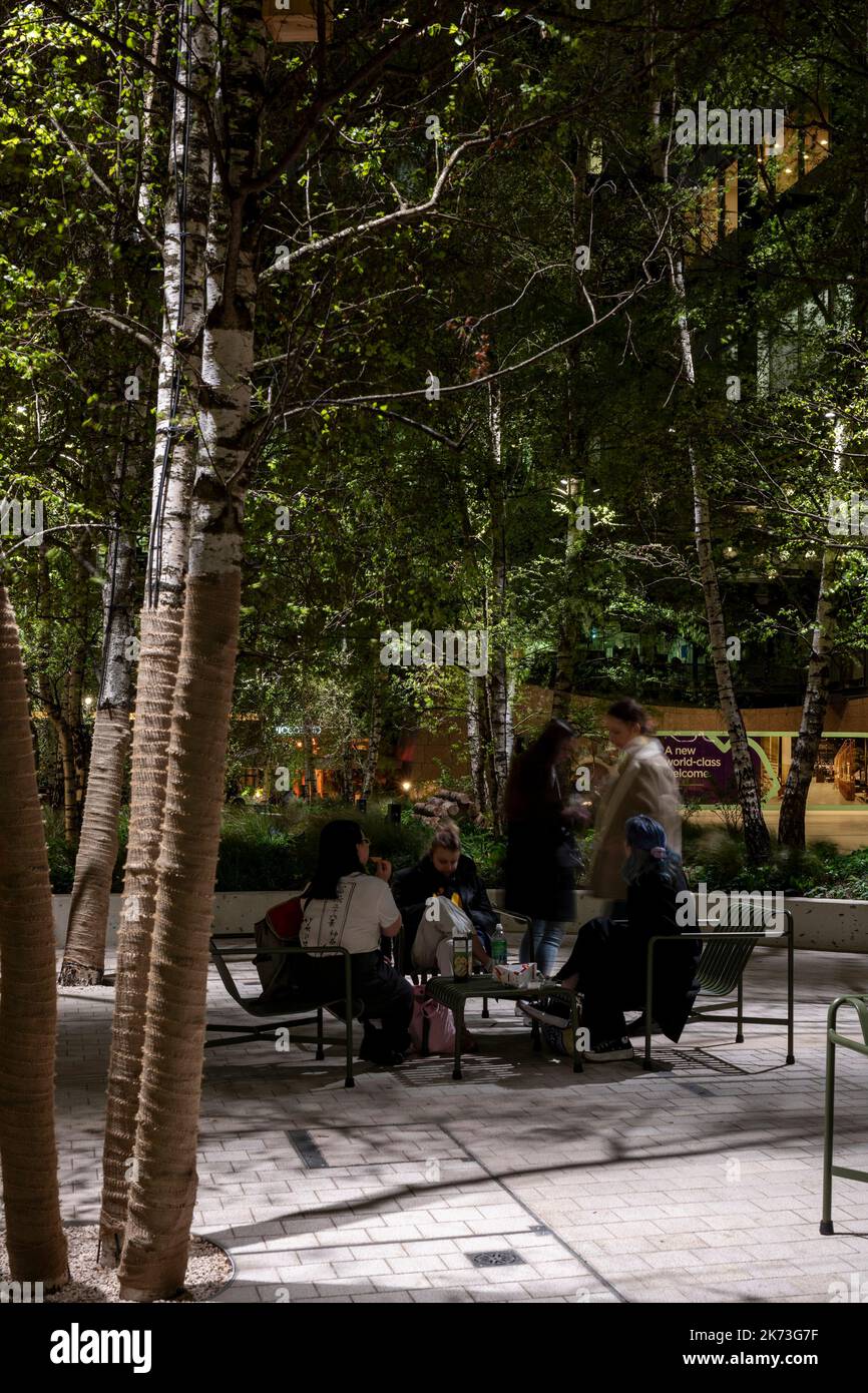 Seating area below trees with white dappled lighting. Exchange Square, London, United Kingdom. Architect: DSDHA, 2022. Stock Photo