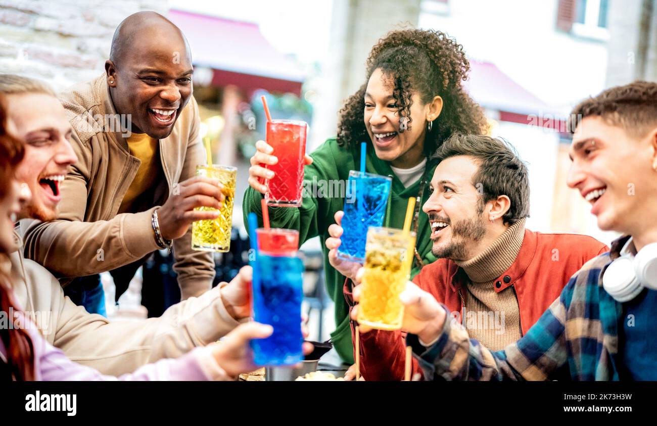 Trendy friends toasting multicolored fancy drinks at bar dehors
