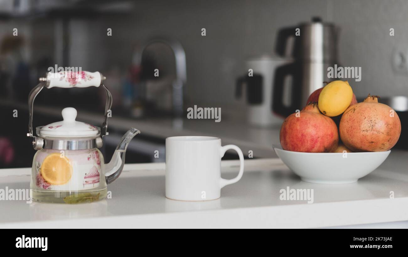 White Mug mockup. white empty mug mockup in a modern kitchen with a hot tea and fresh fruits like pomegranate lemon. Cup mockup that cup sellers Stock Photo