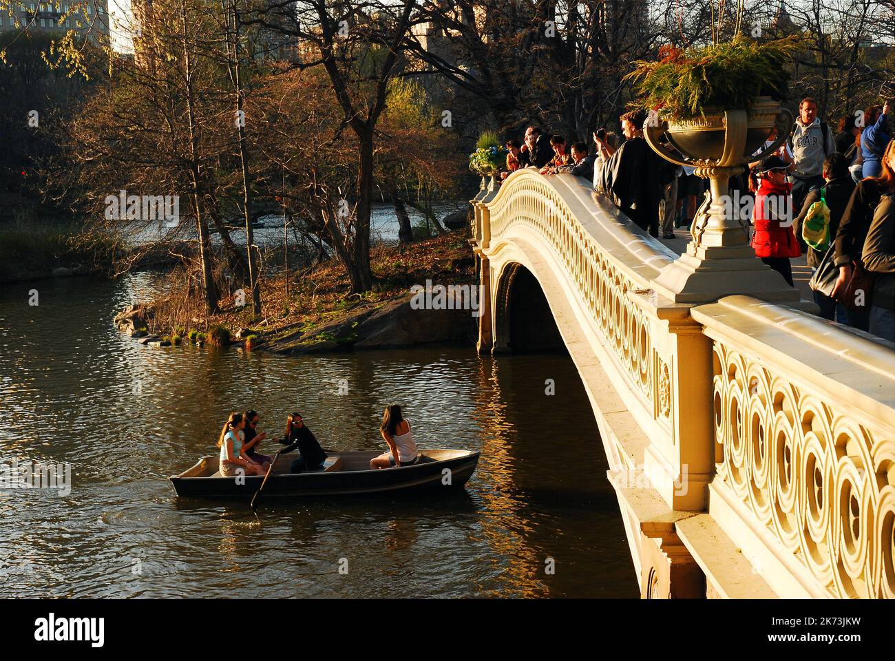 Couples enjoy a warm spring day in a rowboat on the lake in New York Central Park while people on the Bow Bridge take in the view Stock Photo