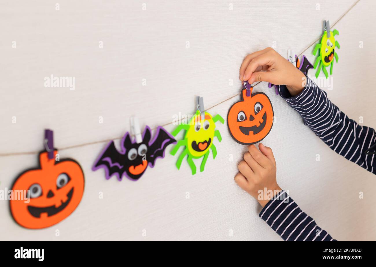 child preparing for Halloween and hanging monsters garland in room Stock Photo