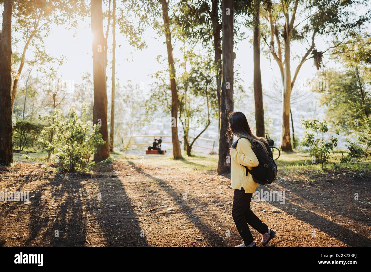 Side view female college student wearing a yellow sweater and a backpack in the campus park road. Innocent smile Stock Photo