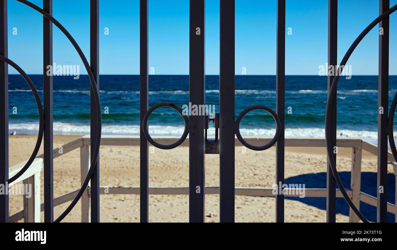 A gate with a lock closes the entrance to the beach with blue sea and sky in the background Stock Photo