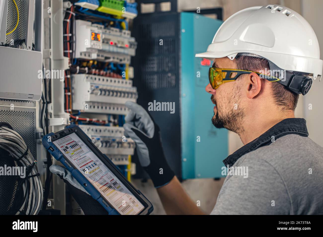 Man, an electrical technician working in a switchboard with fuses. Stock Photo