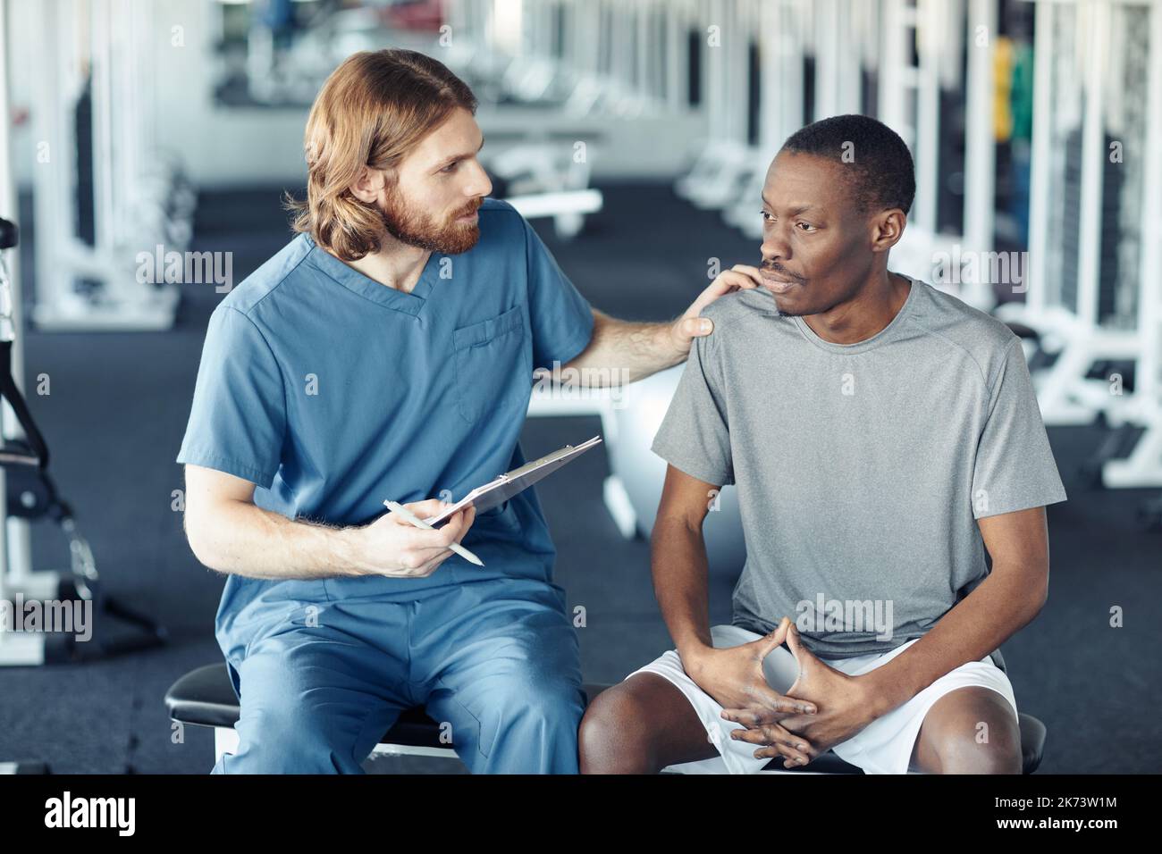 Young doctor in uniform giving recommendation to African patient before sport training in gym Stock Photo