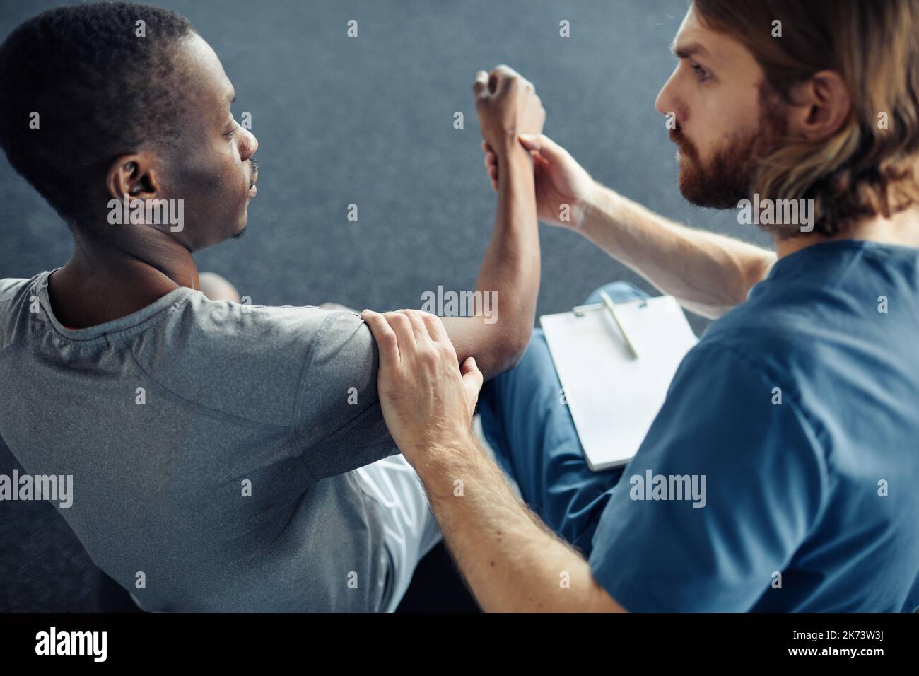 Young male doctor examining pain arm of patient before sport training in gym Stock Photo