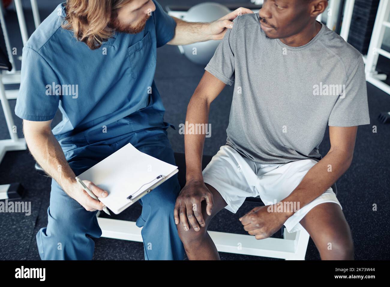 Young doctor in uniform giving recommendation to african male patient before exercising in gym Stock Photo