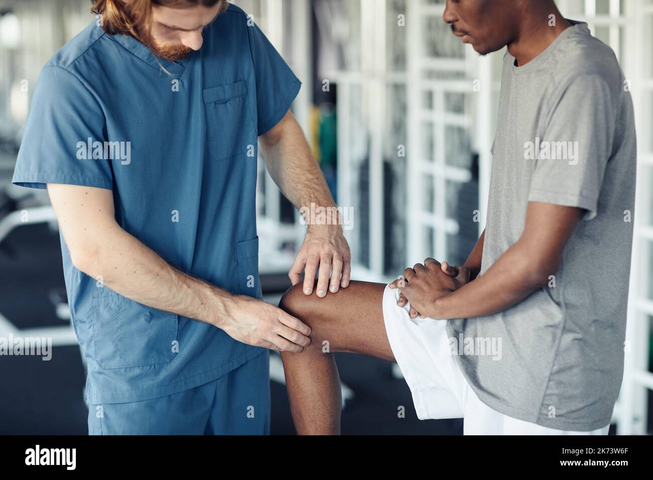 Close-up of doctor in uniform examining the pain leg of African patient in gym Stock Photo