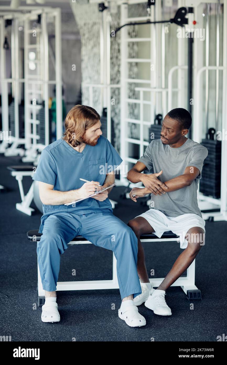 Doctor discussing the way of treatment with patient before sport training in gym Stock Photo