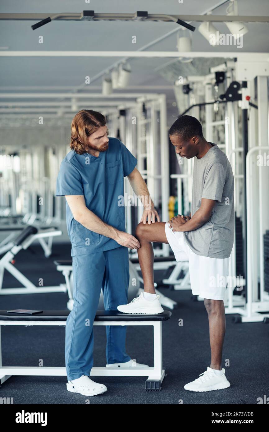 Young doctor in uniform examining patient before sport training in gym Stock Photo