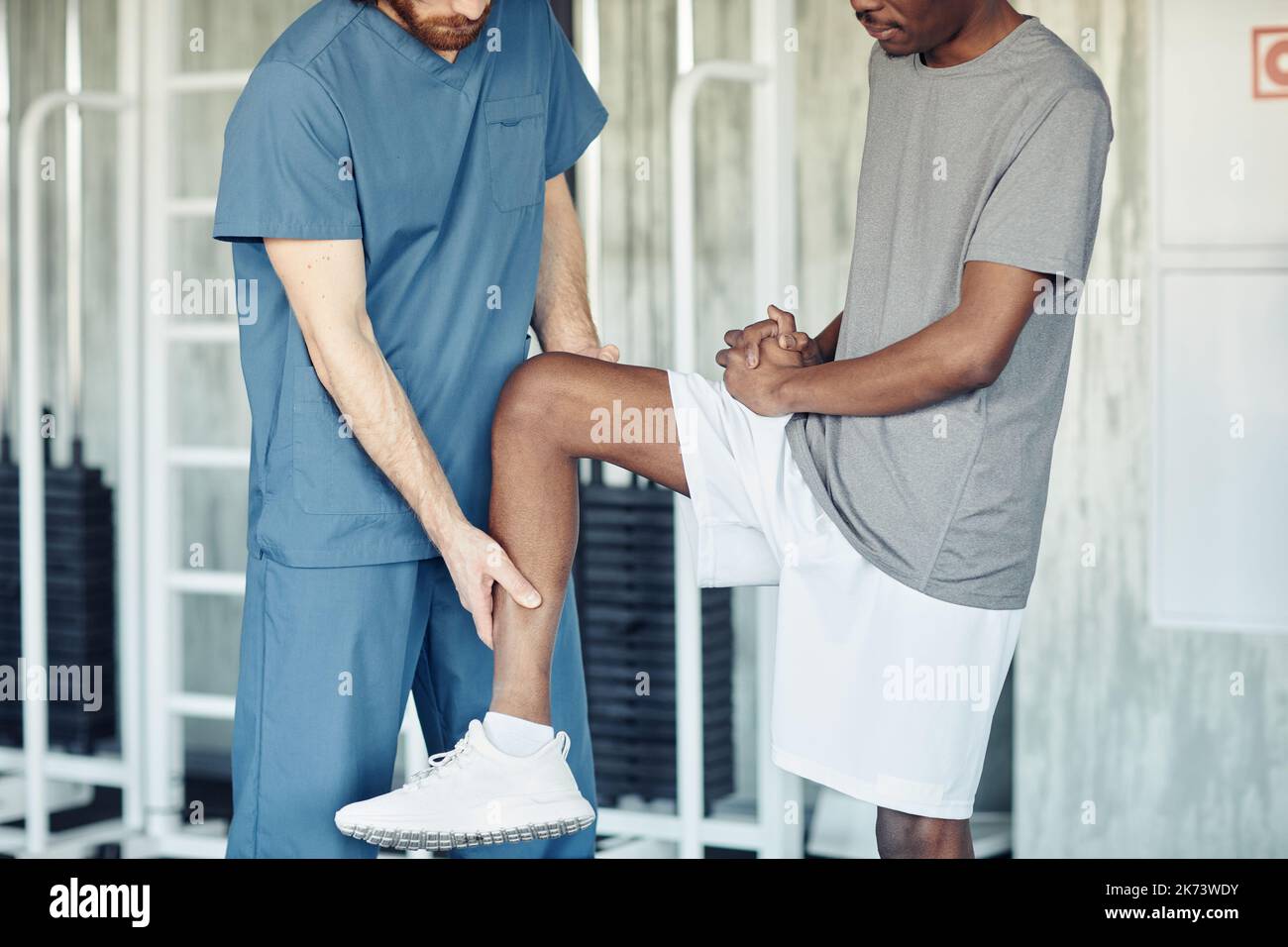 Doctor in uniform examining pain leg of patient in gym before training Stock Photo
