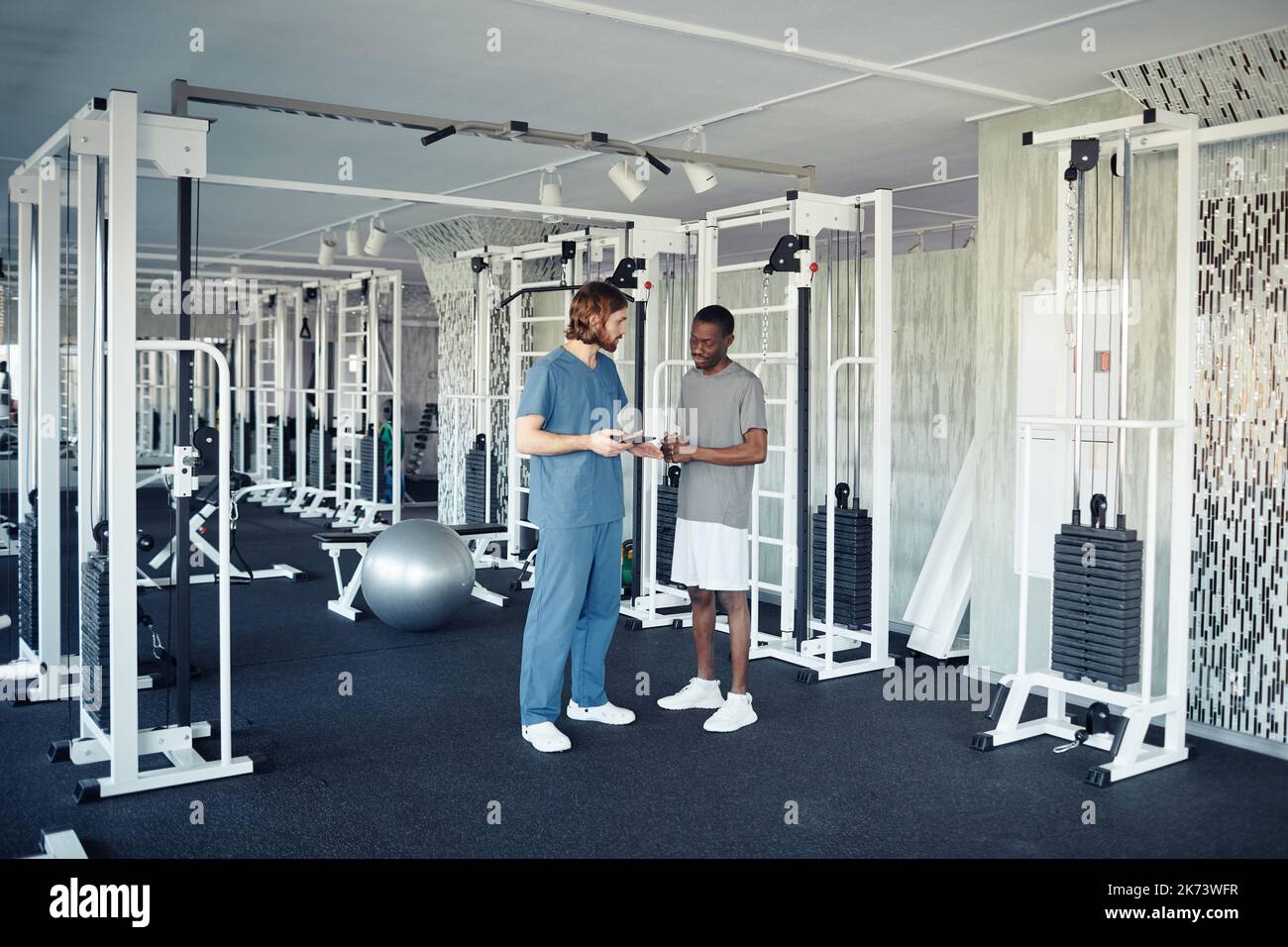 Doctor in uniform controlling sport training of patient while they standing in gym Stock Photo