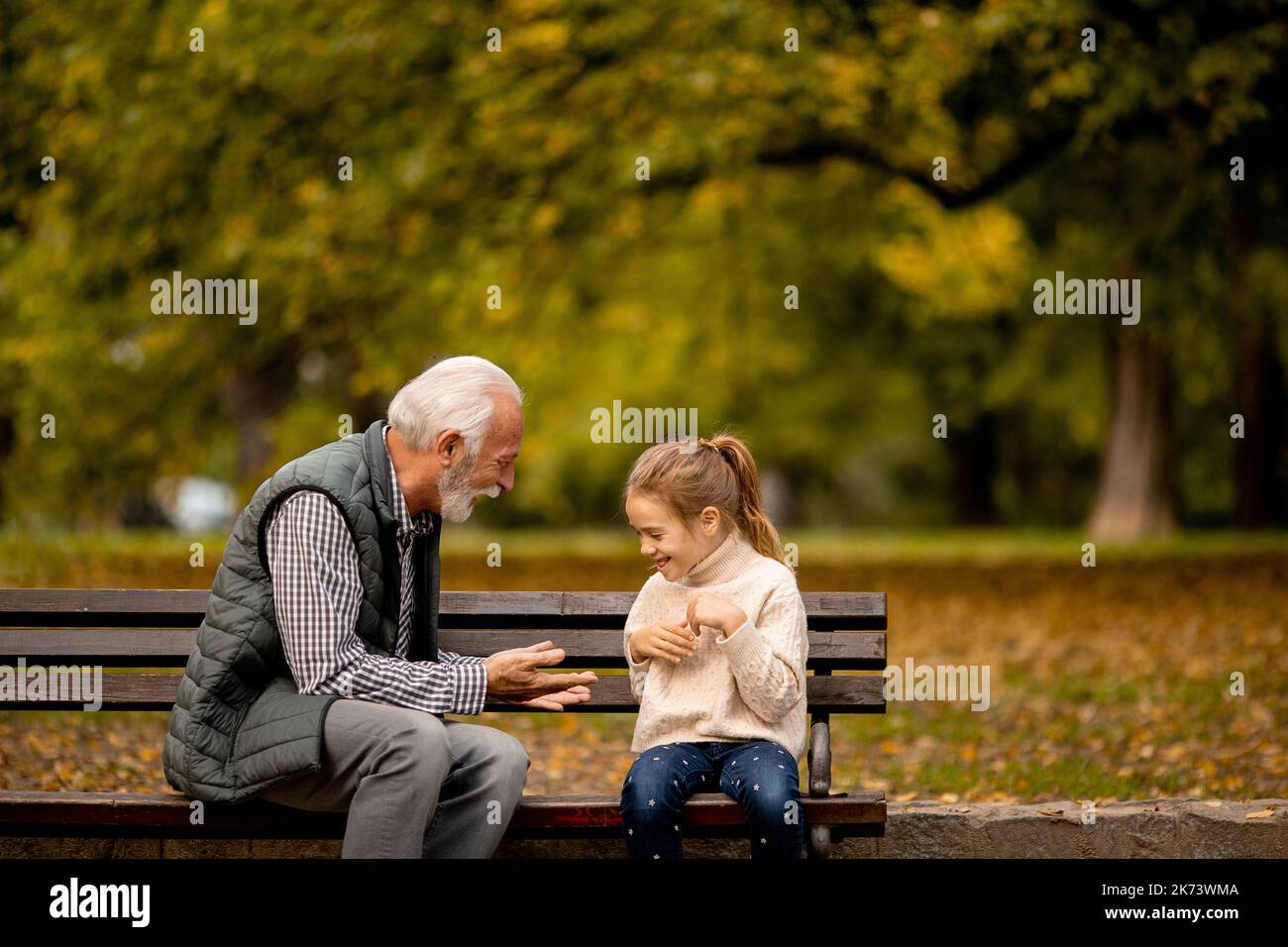 Handsome grandfather playing red hands slapping game with his granddaughter in park on autumn day Stock Photo