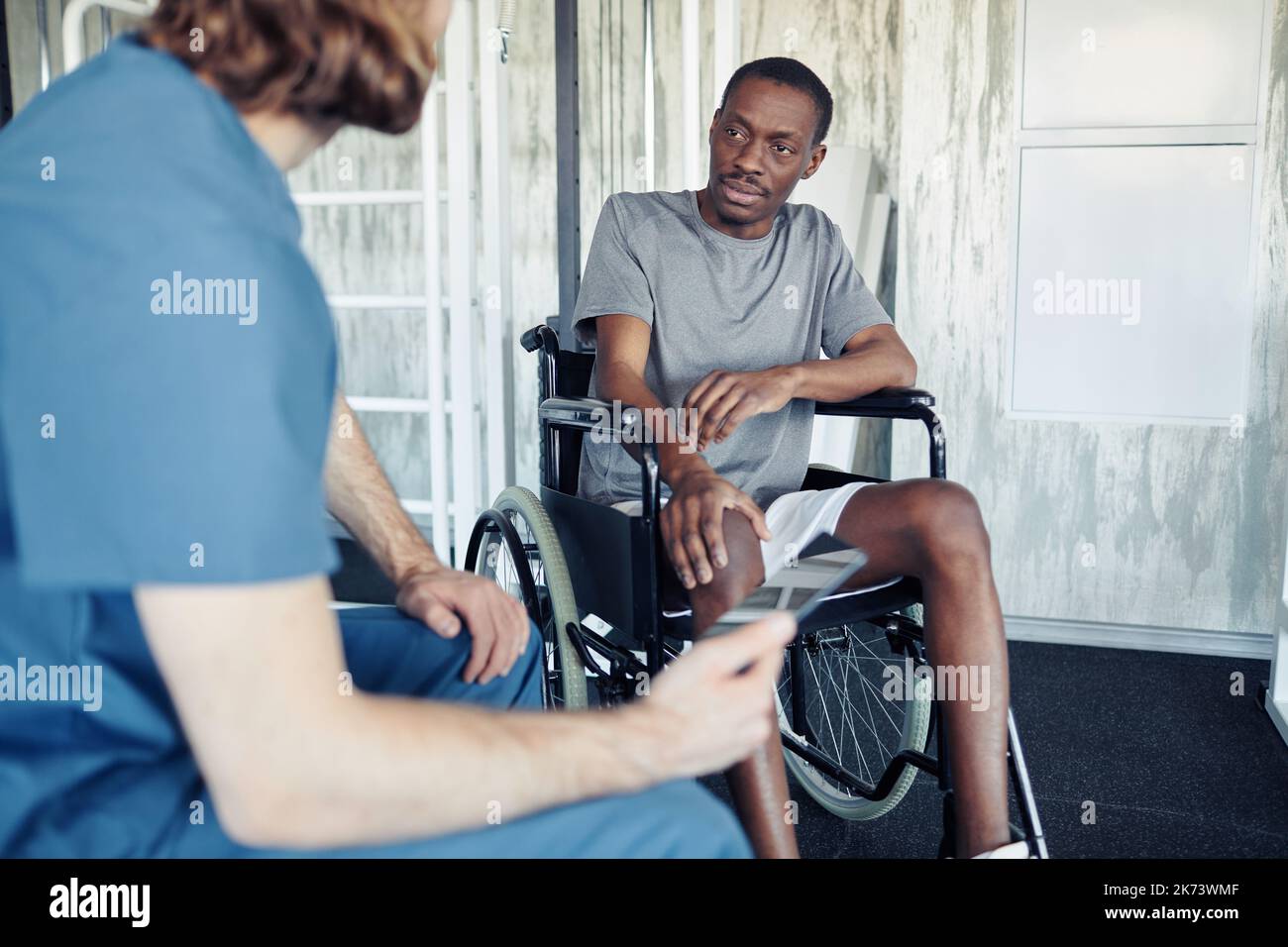 African patient sitting in wheelchair and talking to doctor about his rehabilitation in gym Stock Photo