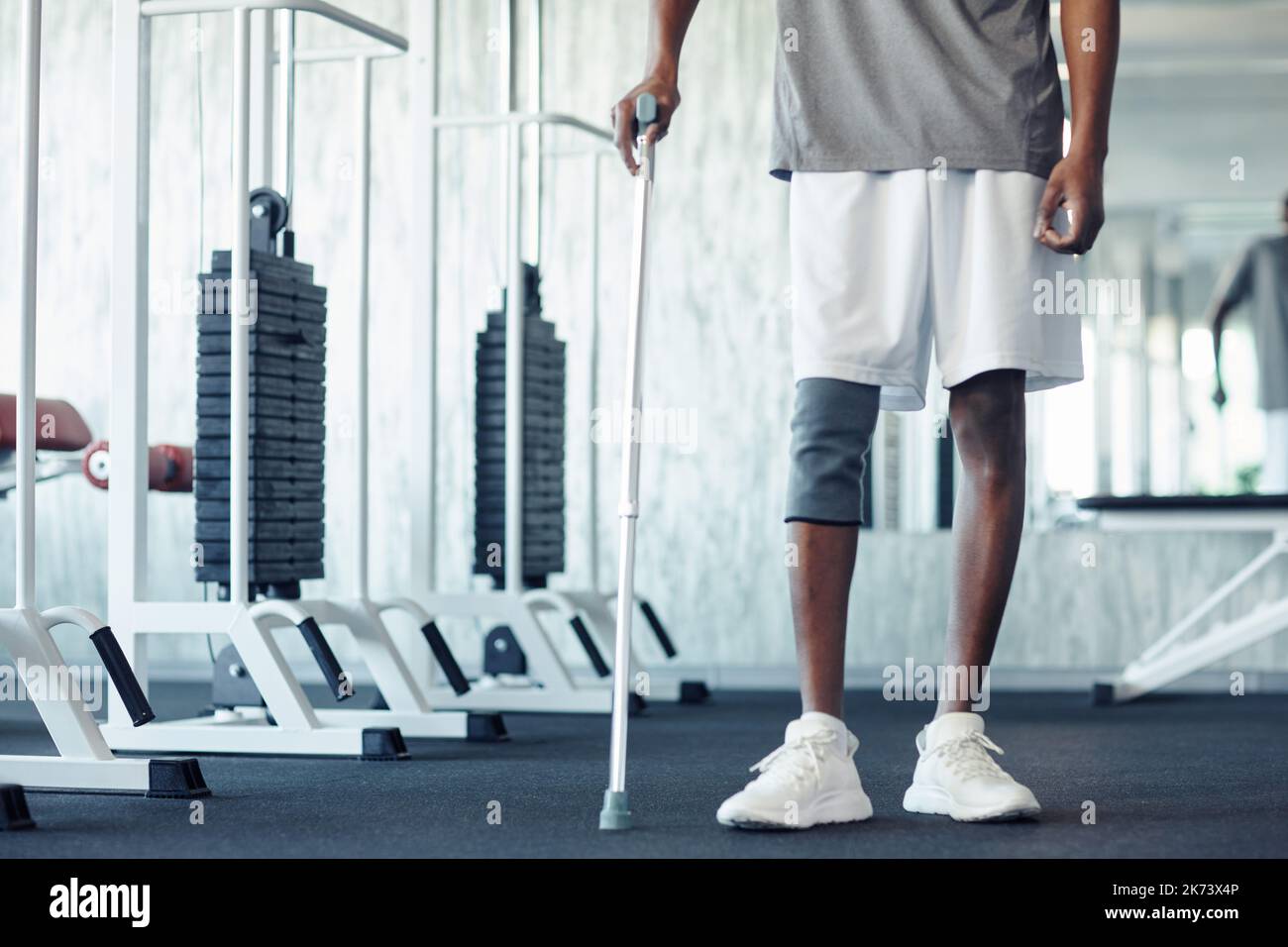 Close-up of African patient walking with walking stick along gym, he holding rehabilitation with his injury leg Stock Photo