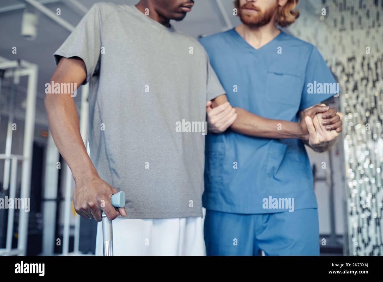Close-up of doctor in uniform holding hand of patient and helping him to walk during rehabilitation in gym Stock Photo