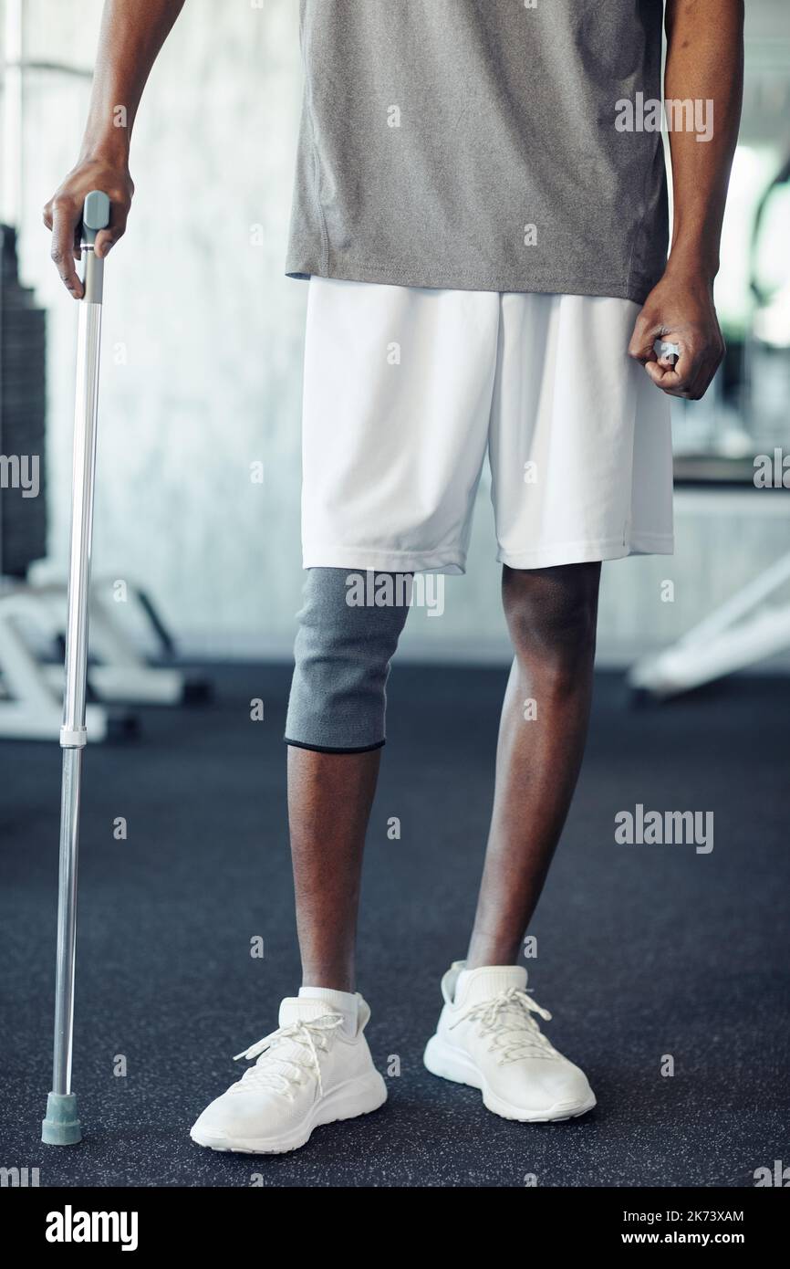 Close-up of African athlete with injury leg walking with walking stick in gym during his sport exercising Stock Photo
