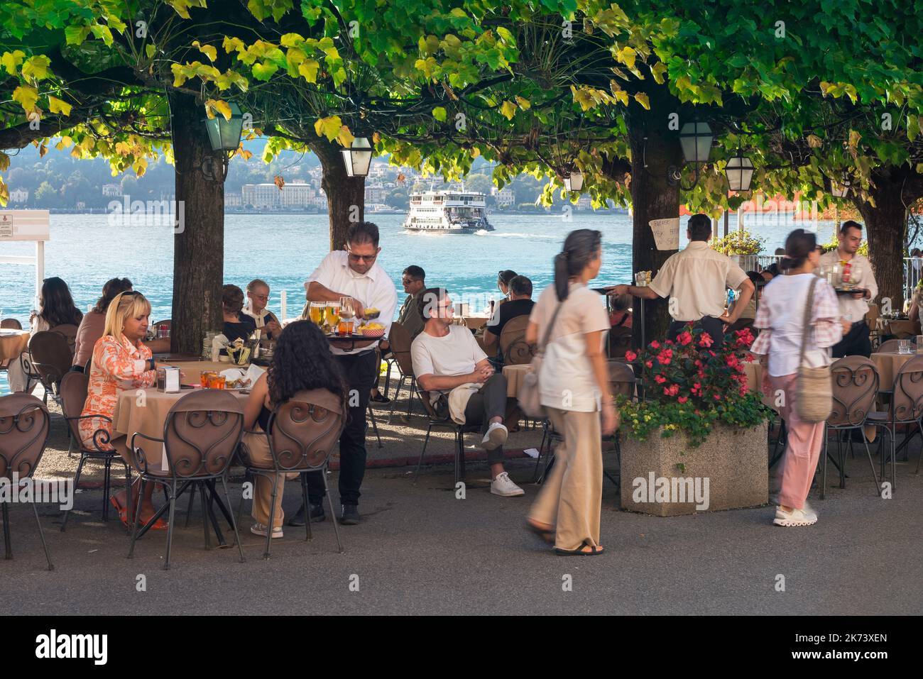 Bellagio Italy restaurant, view in summer of people relaxing on the terrace of a lakeside restaurant in the Piazza Mazzini in Bellagio, Lake Como Stock Photo