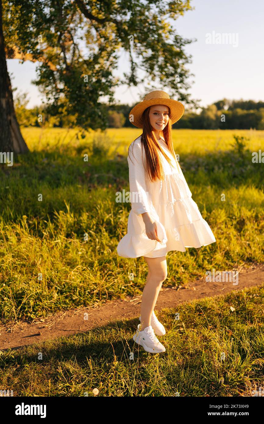 Vertical portrait of smiling red-haired young woman in straw hat and ...