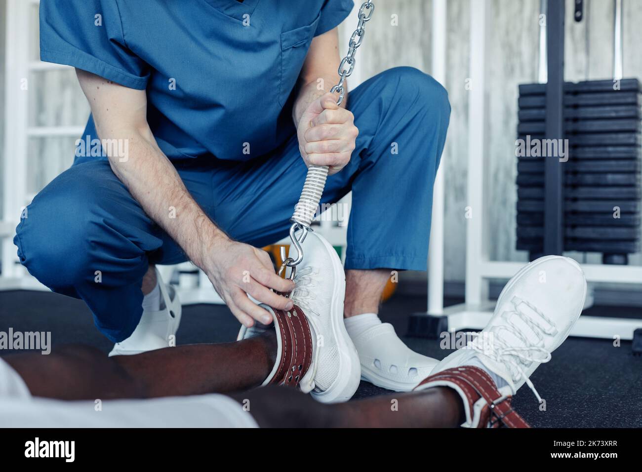 Close-up of doctor in uniform wearing sport equipment on legs of patient during sports training in gym Stock Photo