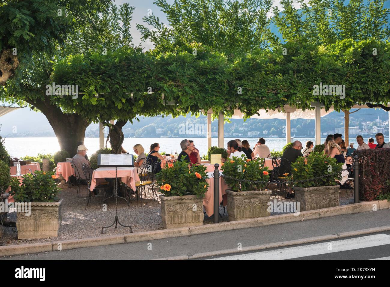 Bellagio Italy restaurant, view in summer of people relaxing on the terrace of a lakeside restaurant in the Piazza Mazzini in Bellagio, Lake Como Stock Photo