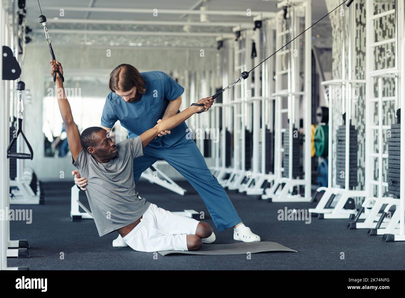 African patient doing stretching exercises together with doctor during sport training in gym Stock Photo