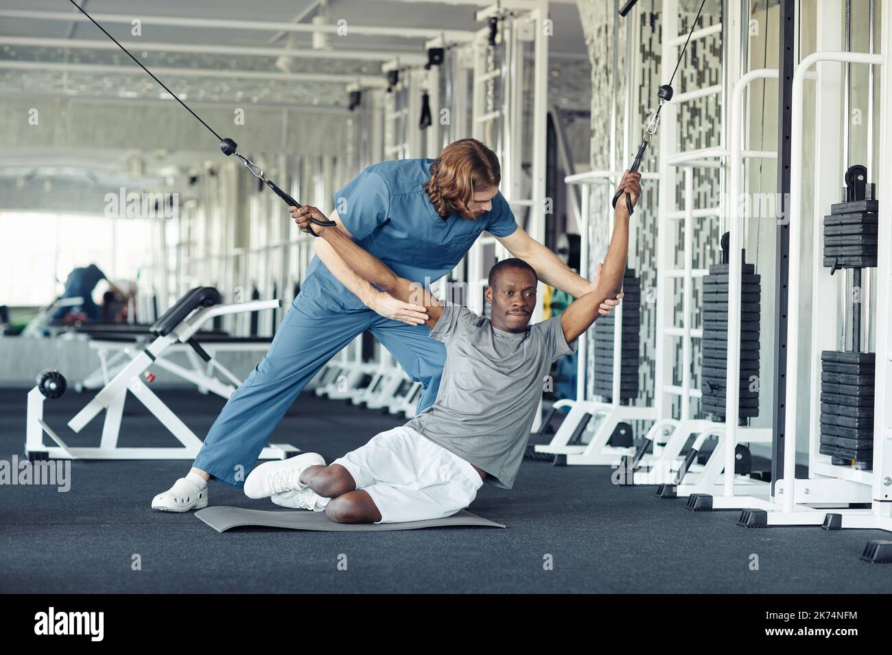 Young doctor in uniform helping patient with stretching exercises during training in gym Stock Photo