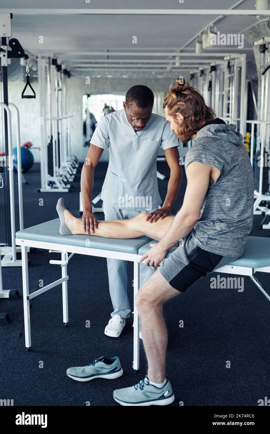 African young therapist massaging leg of patient before sport training in gym Stock Photo