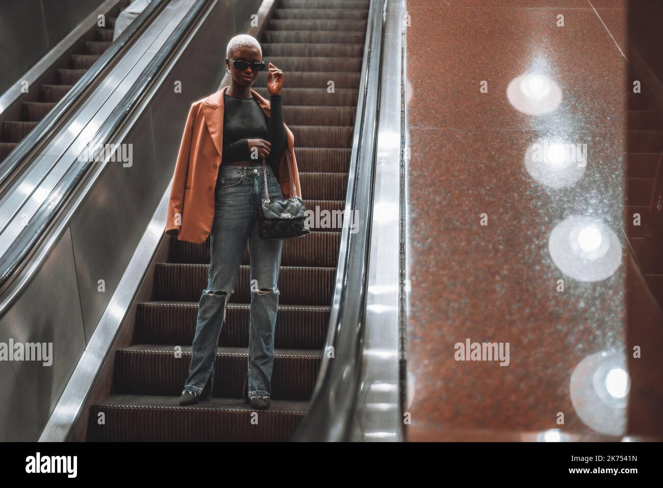 A young fashionable black female on the moving staircase descending to