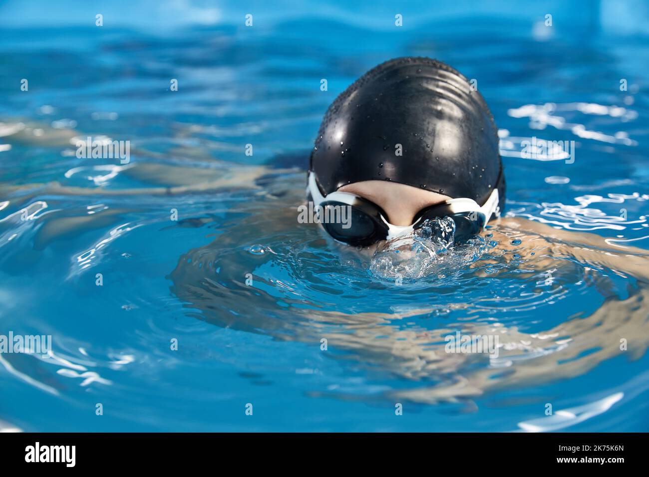 Preschool boy learning how to swim in a pool wearing swimming cap and