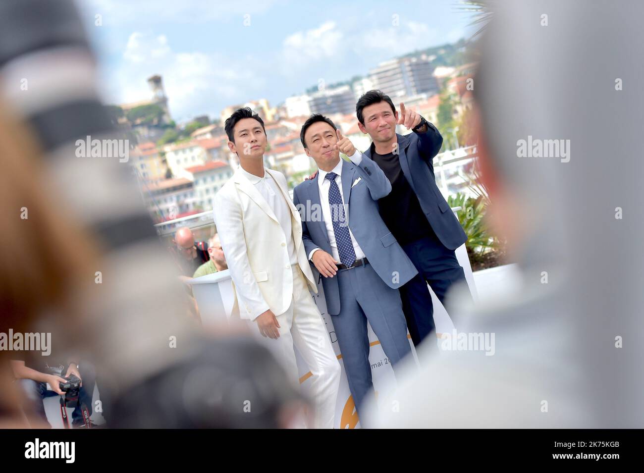 (R-L) Actors Ji-Hoon Ju waves as Sung-min Lee gives the thumbs up as Jung-min Hwang attends the photocall for 'The Spy Gone North (Gongjak)' during the 71st annual Cannes Film Festival at Palais des Festivals on May 11, 2018 in Cannes, France. Stock Photo
