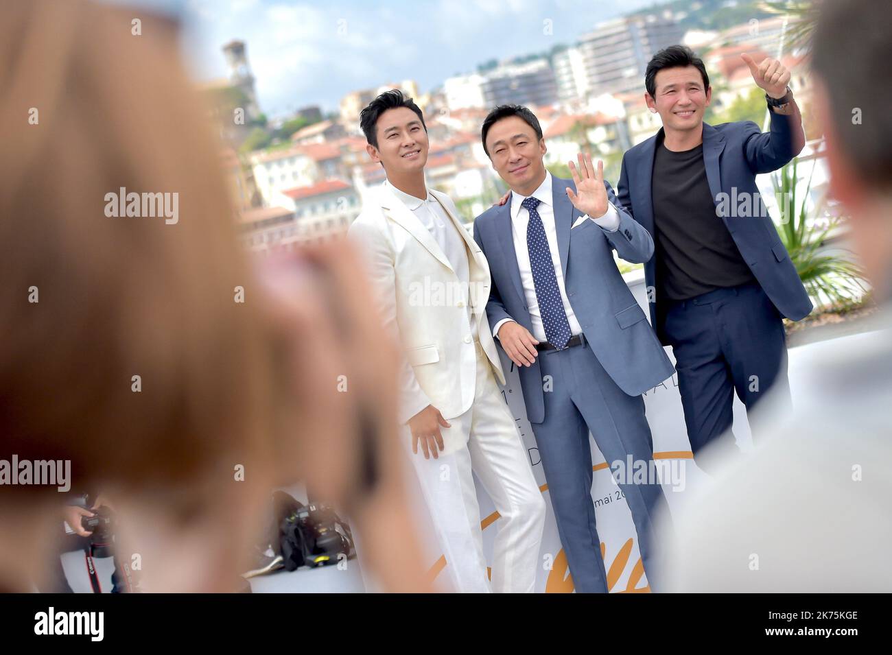 Actors Ji-Hoon Ju waves as Sung-min Lee gives the thumbs up as Jung-min Hwang attends the photocall for 'The Spy Gone North (Gongjak)' during the 71st annual Cannes Film Festival at Palais des Festivals on May 11, 2018 in Cannes, France. Stock Photo