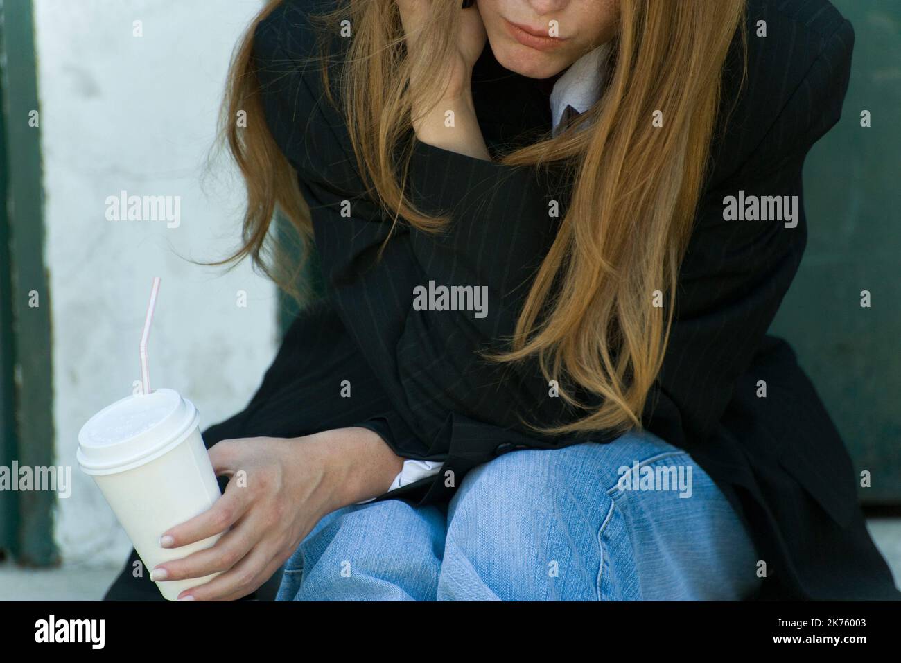 A young woman leaning on her elbow holding a cup with a plastic straw. Stock Photo