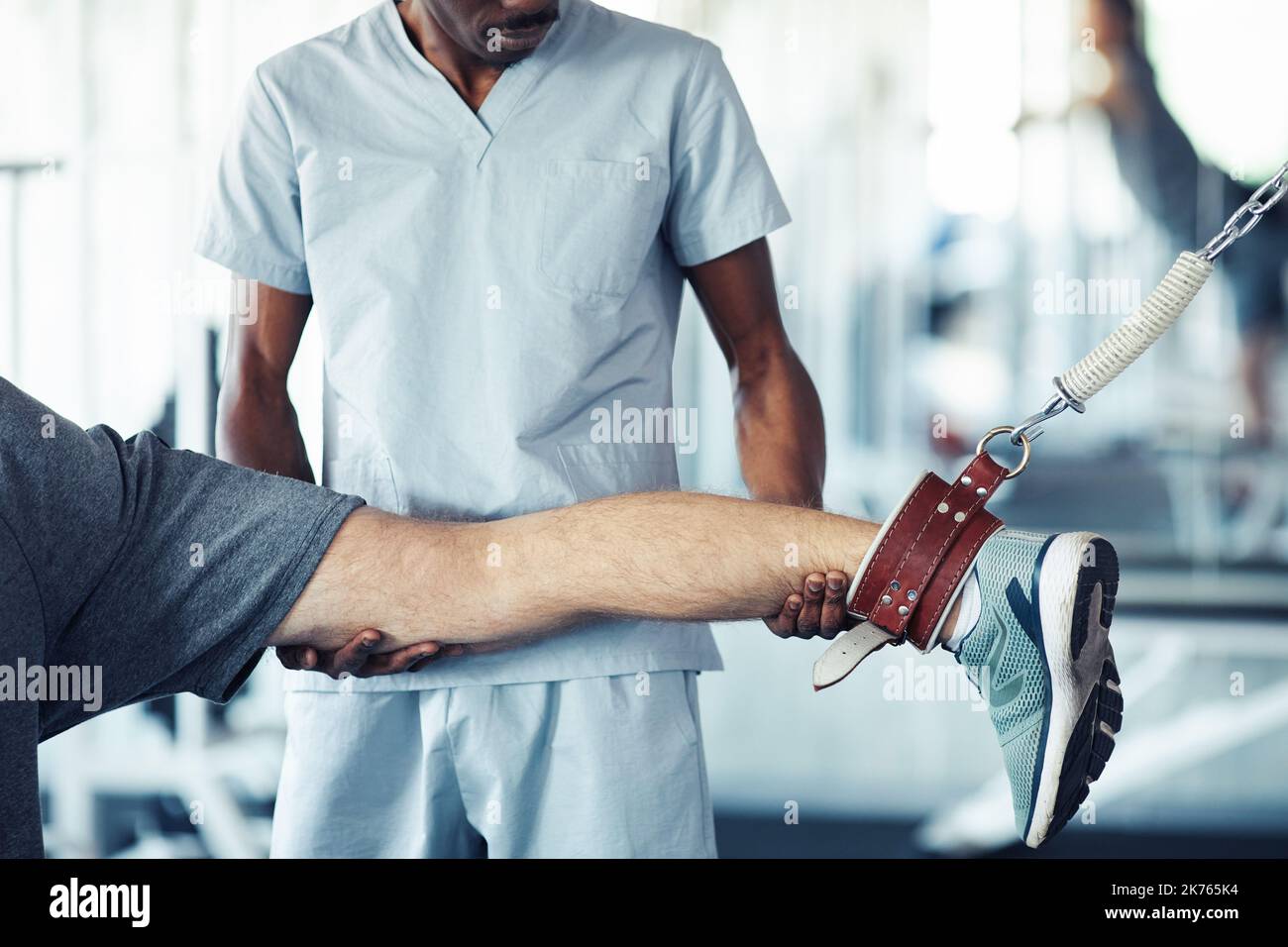 Close-up of therapist in uniform holding leg of patient while he doing stretching exercises in gym Stock Photo