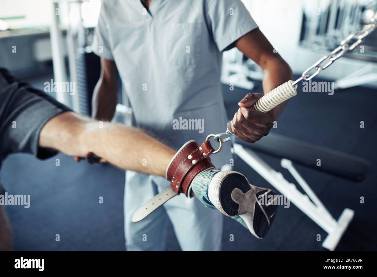 Close-up of patient training his leg on sport equipment together with nurse supporting him during their exercises in gym Stock Photo