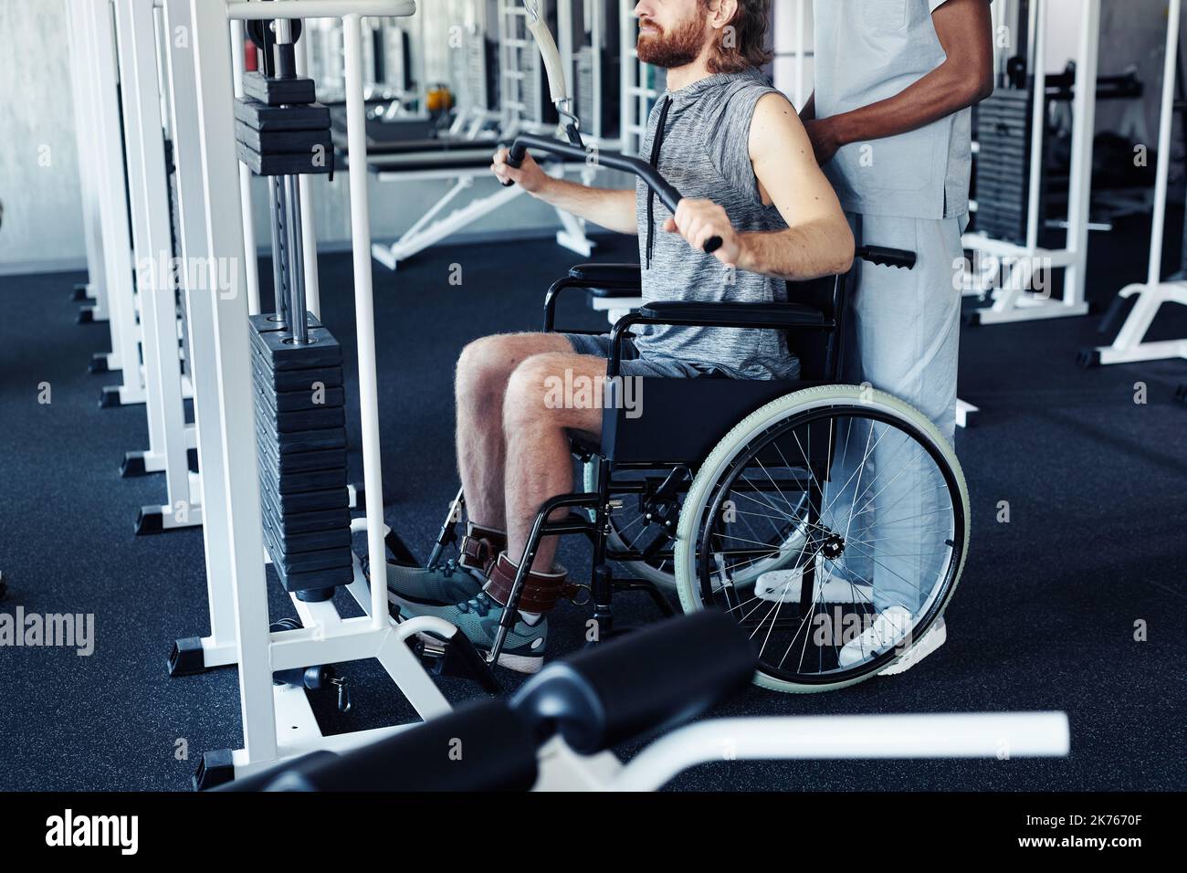 Young patient with disability sitting in wheelchair and training his back with sport equipment